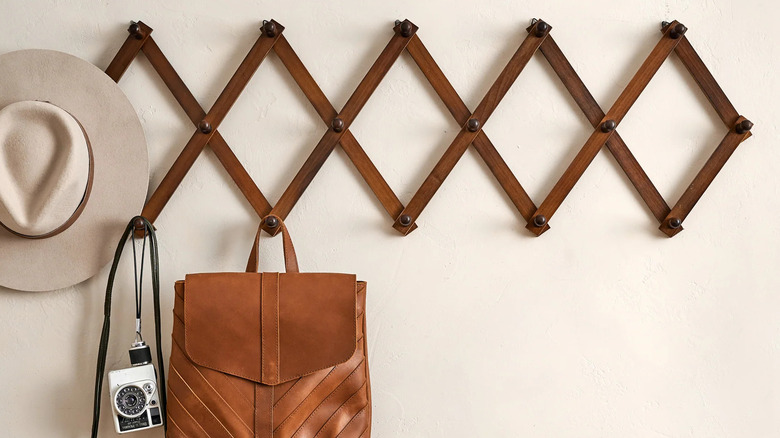 A wooden accordion wall hook holds a taupe hat, vintage camera, and leather bag