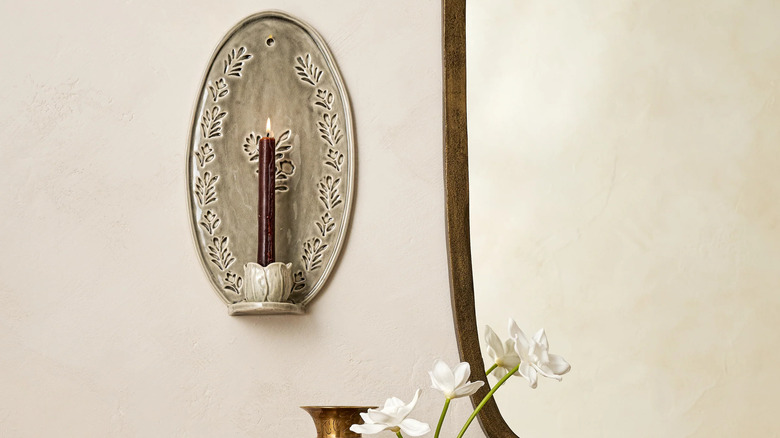 A floral ceramic wall scone holds a burgundy tapered candle