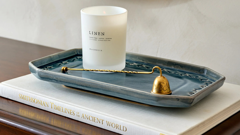 A linen-scented candle and flame snuffer sit on a blue ceramic tray