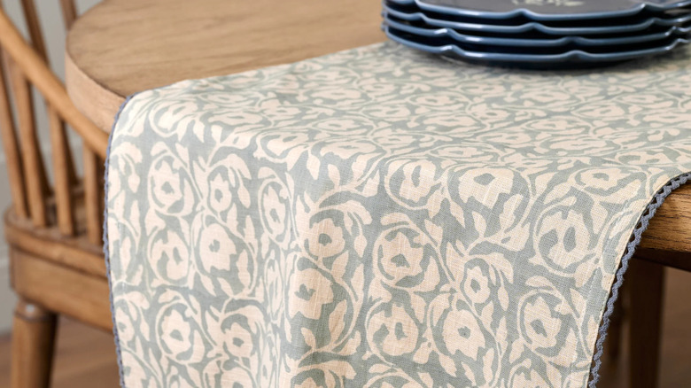 A soft blue and cream patterned table runner sits on a light wooden table