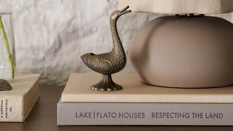 A duck-shaped brass tapered candle holder sits on a pile of books