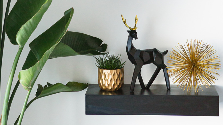 thick black floating shelf with gold potted plants and greenery to the side