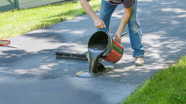 Person pouring asphalt sealant on a driveway