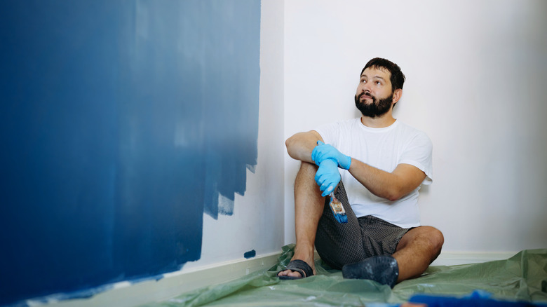 A person taking a break from painting a room dark blue
