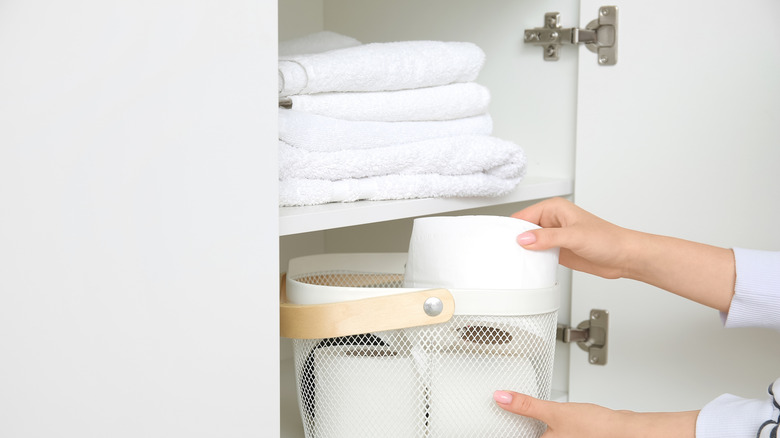 Person grabbing a roll of toilet paper out of a metal basket in a closet