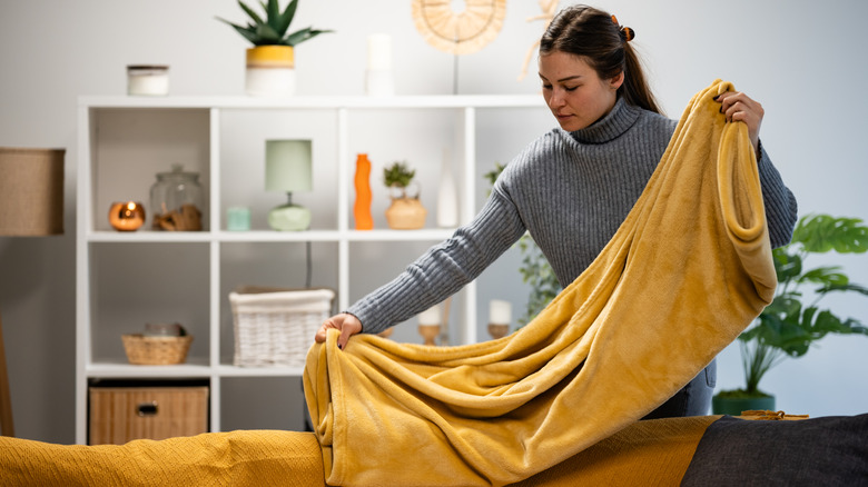 Woman folding up a yellow blanket in a living room