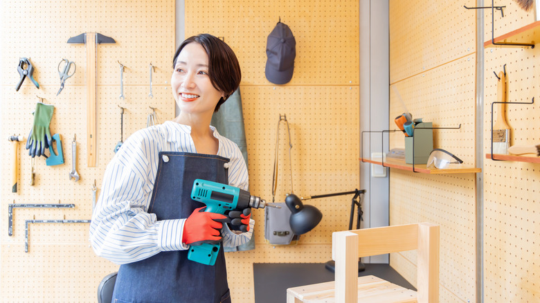 A woman holds a drill and smiles