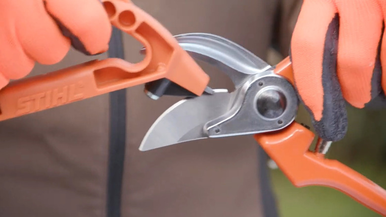 A person sharpening a pruning tool with a STIHL 3-in-1 sharpening tool