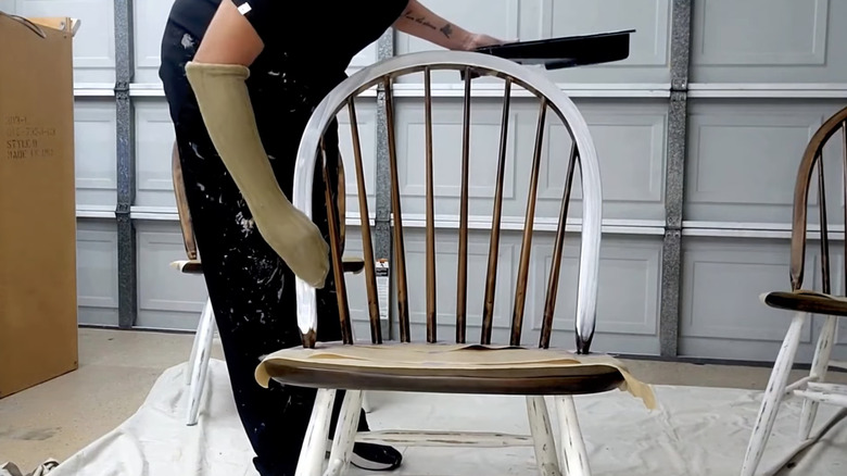 person painting chair with sock on hand