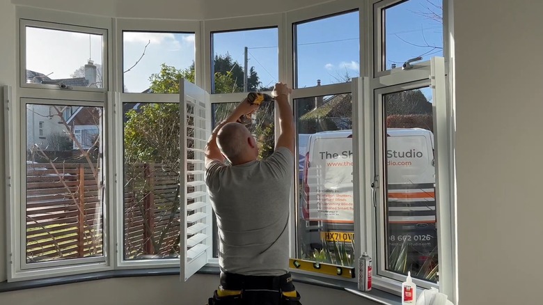 Man installing cafe shutters to cover a living room window