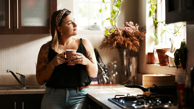 Woman drinking coffee and looking out kitchen window
