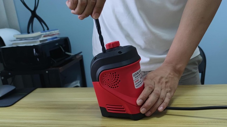 Hands grinding a drill bit with the red electric drill bit sharpener on a table top