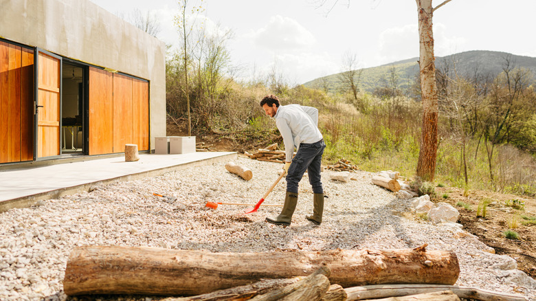 Person using rake to tidy gravel landscaping in front of modern house