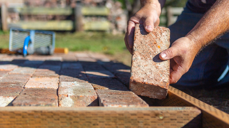 Person laying reclaimed brick into outdoor walkway path