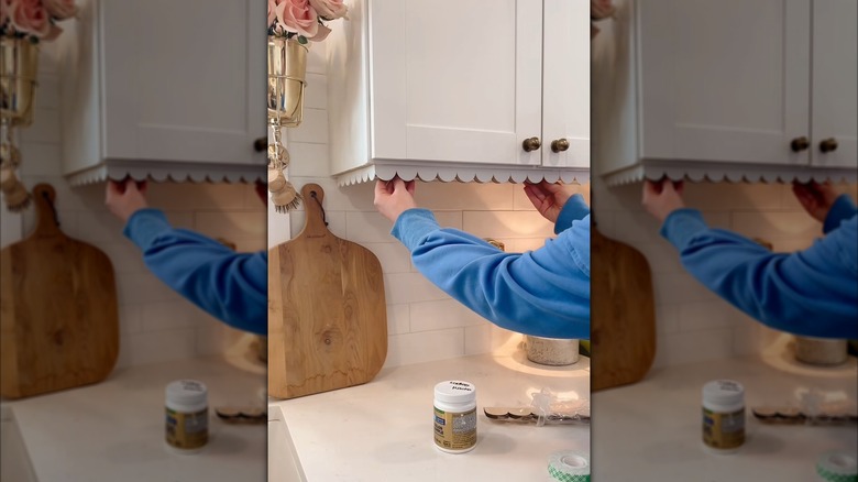 a DIYer places decorative trim underneath a kitchen cabinet