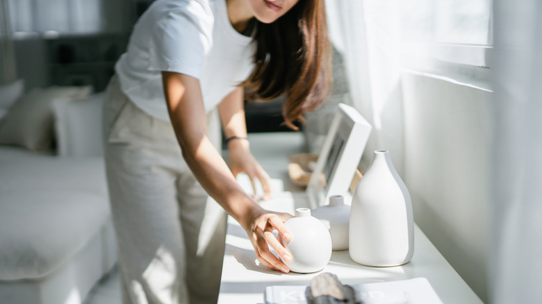 Woman placing white colored home decor items on a shelf