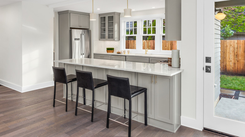 A kitchen peninsula in a small, modern, and sleek kitchen with a small view of the backyard