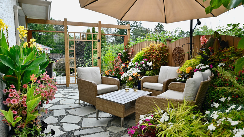 a wicker patio set sits on a gray stone and gravel patio surrounded by flowering plants