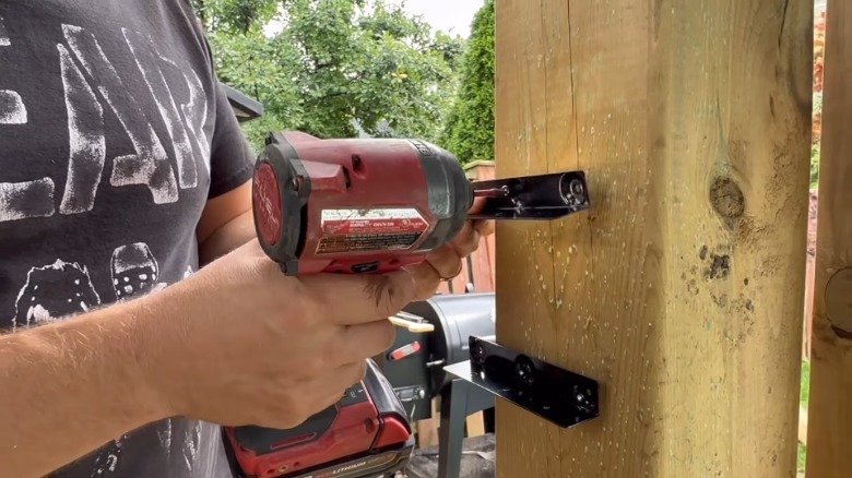 Man drilling shutter brackets into wood post.