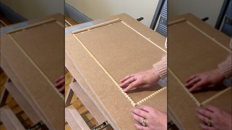Woman arranging wooden beads as unique cabinet trim for plain Shaker cabinets in home DIY