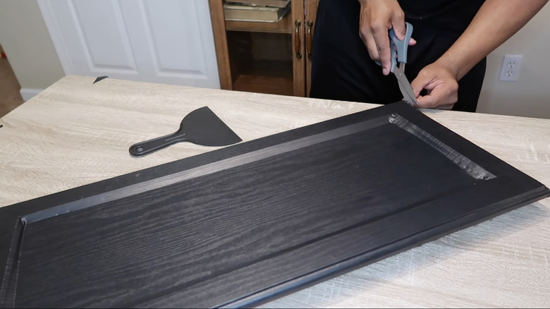 Trimming peel-and-stick wallpaper on a cabinet