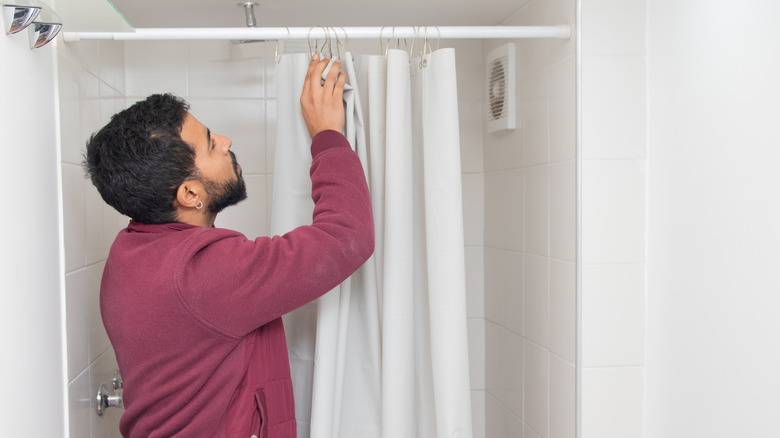 Person touching the rings on white curtain hanging on a shower rod