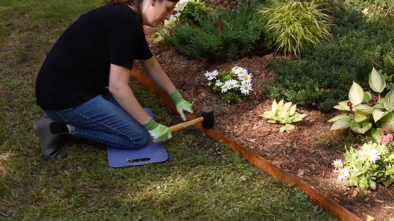 A woman hammers a piece of Cor-ten steel garden edging into the ground