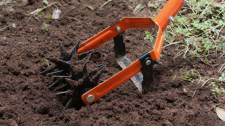 An orange Walnesee Rotary Cultivator is used to aerate garden soil