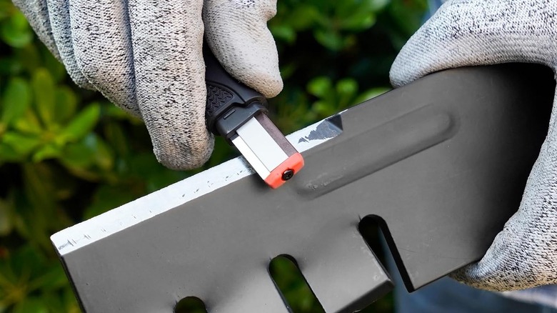 a person using the SHARPAL 129N garden tool blade sharpener on mower blades