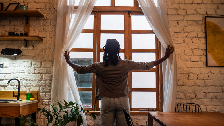 Woman opening curtains in front of kitchen window