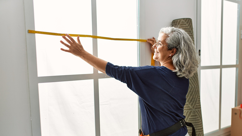 A smiling woman measuring a window