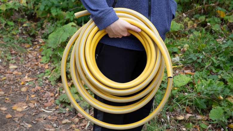 A person carrying a rolled-up yellow garden hose