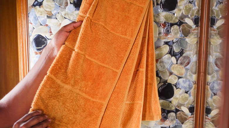 A person holding an orange bath towel in front of a piece of wall decor made from smooth rocks