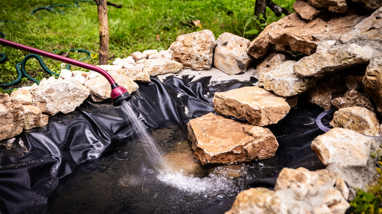 A DIY pond surrounded by large rocks and is being filled with water