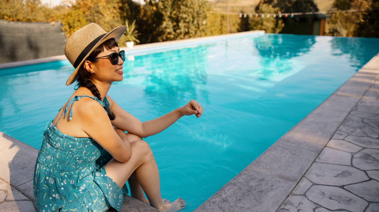 A woman sitting by a swimming pool in the backyard of a home