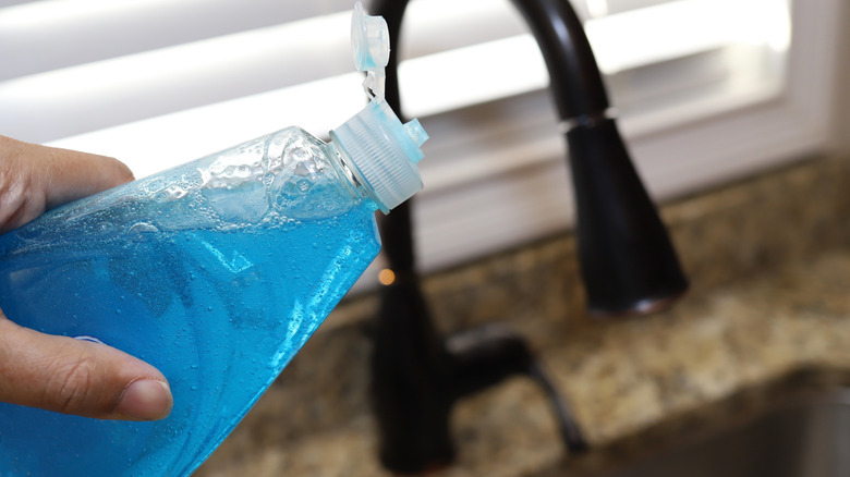 Someone holding a bottle of blue dish soap