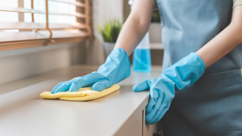 A person wearing blue gloves cleans counter tops with a yellow rag
