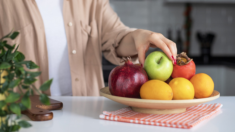 Person arranging fruit on a basic fruit bowl in a kitchen