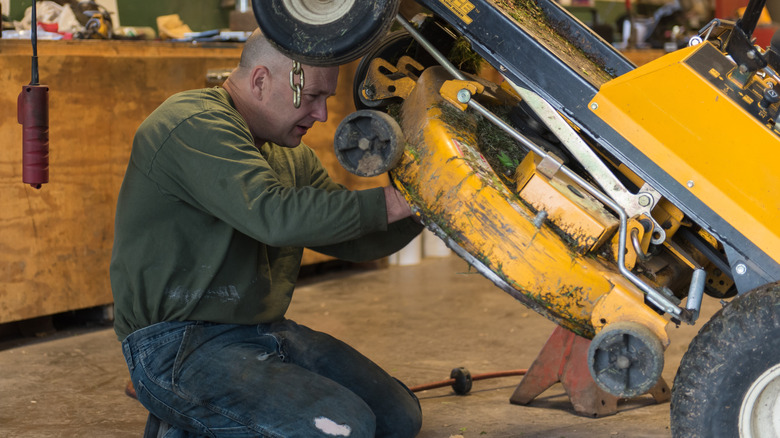 Man removing blades of yellow mounted zero-turn lawn mower