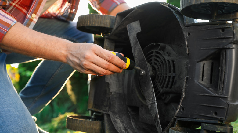 Man screwing off a push mower blade with a yellow screwdriver