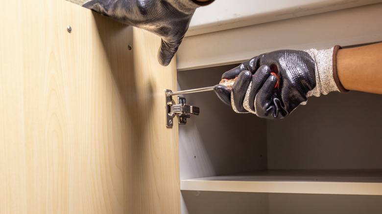 Person unscrewing the hinges on a kitchen cabinet