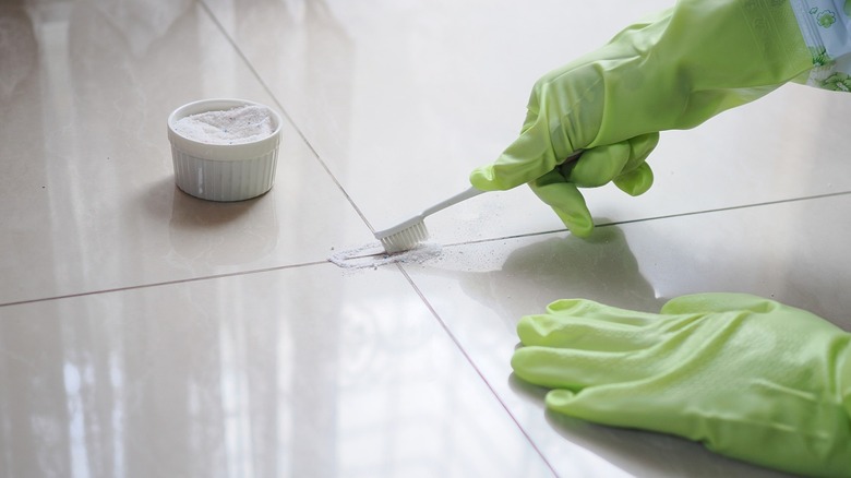Person wearing rubber gloves cleaning tile grout with a toothbrush