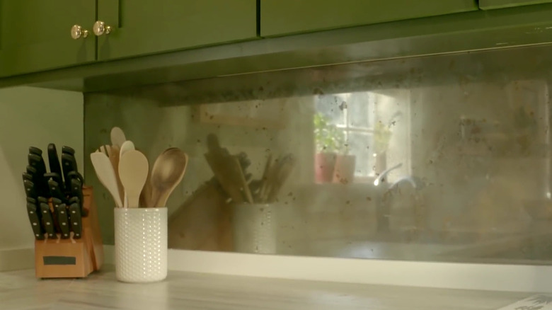 A kitchen with green cabinets and a mercury glass-effect backsplash.