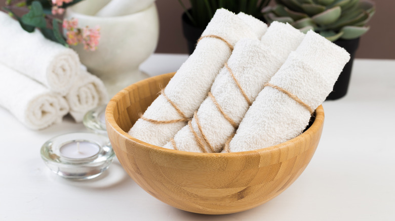 Rolled white hand towels in a bamboo bowl