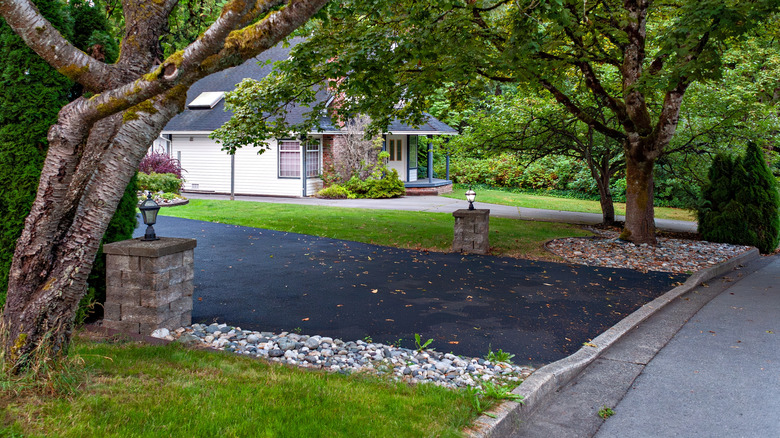 Asphalt driveway surrounded by trees and decorative stones