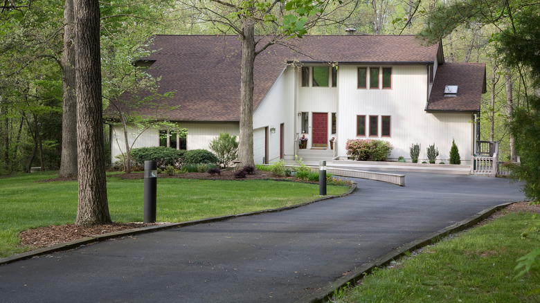 An elegant, modern home with a blacktop asphalt driveway and a wooded yard