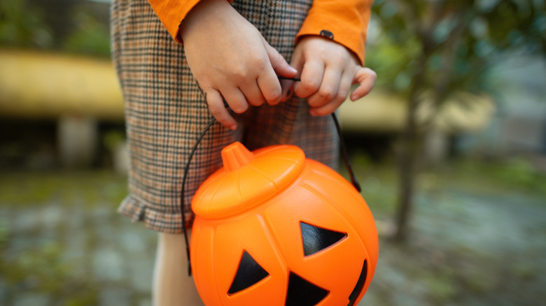 A person holding a plastic Halloween pumpkin basket.