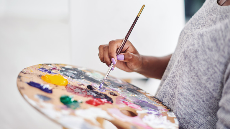 A woman with a lilac manicure holds a paint palette