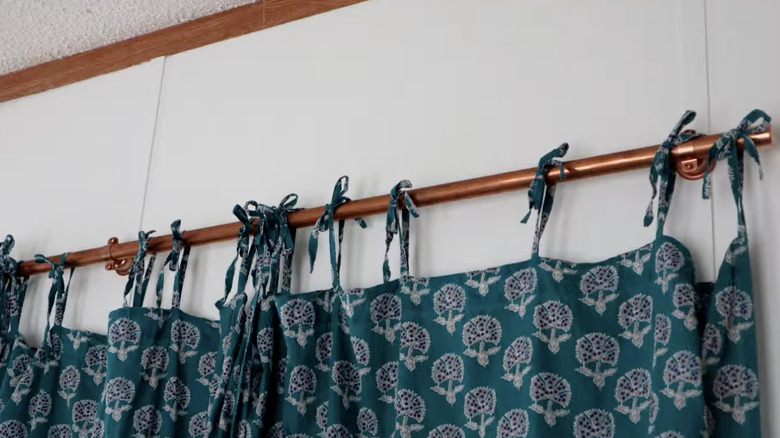 A copper rod being used as a curtain rod holding a blue patterned curtain