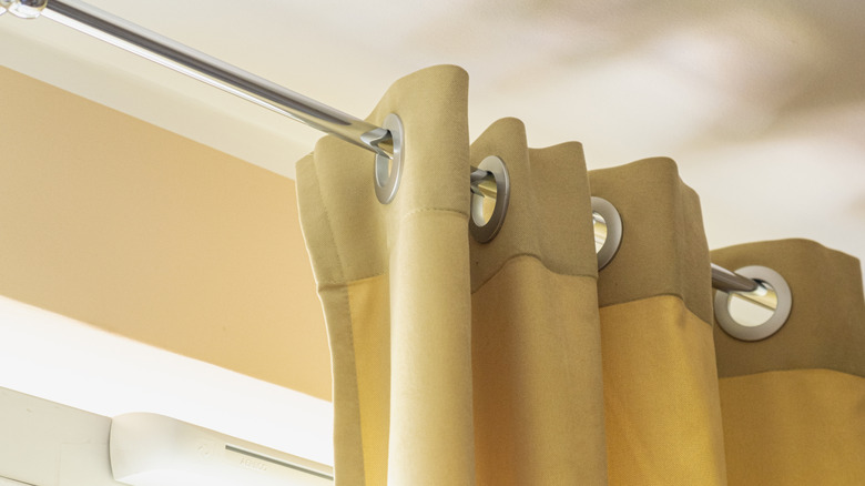 A yellow curtain hangs on a silver curtain rod